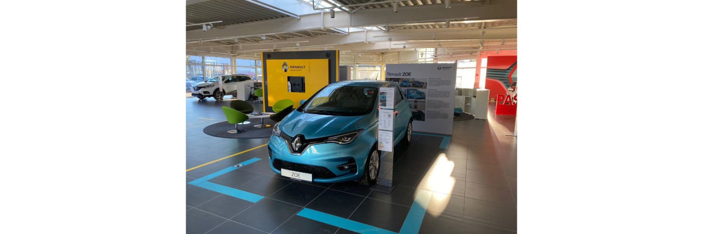 Ein blauer Renault ZOE in einem modernen Autohaus mit Produktinformationen im Hintergrund.