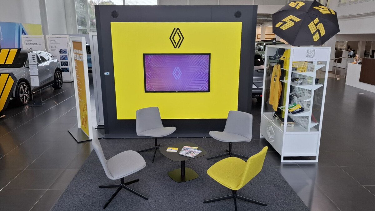 Renault-Ausstellungsbereich mit gelbem Hintergrund, Fernseher, Sitzgruppe und Verkaufsständen.