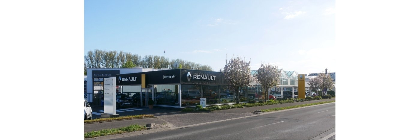 Renault Autohaus an einer Straße, umgeben von Bäumen und frühlingshaften Blüten. Klare Sicht auf das Gebäude.