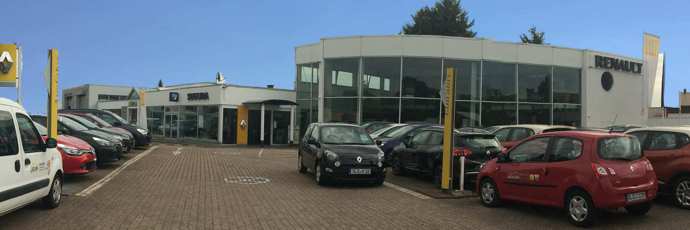 Renault Autohaus mit mehreren Autos auf dem Parkplatz, modernes, gläsernes Gebäude im Hintergrund.