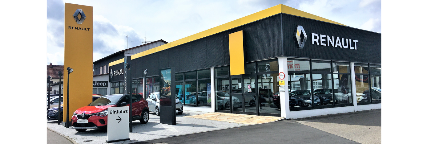 Renault Autohaus mit gelber Fassade und rotem Auto vor dem Eingang, Parkplatz und Schilder sichtbar.