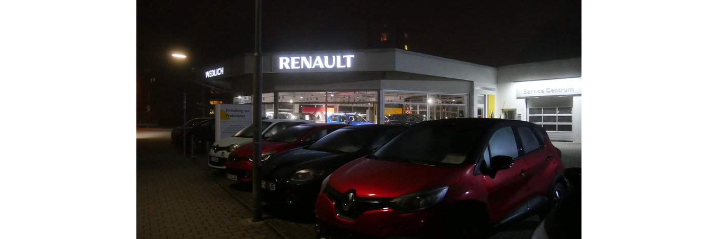 Renault Autohaus bei Nacht, mit mehreren Autosparkt, beleuchtet von der Verkaufsfläche.