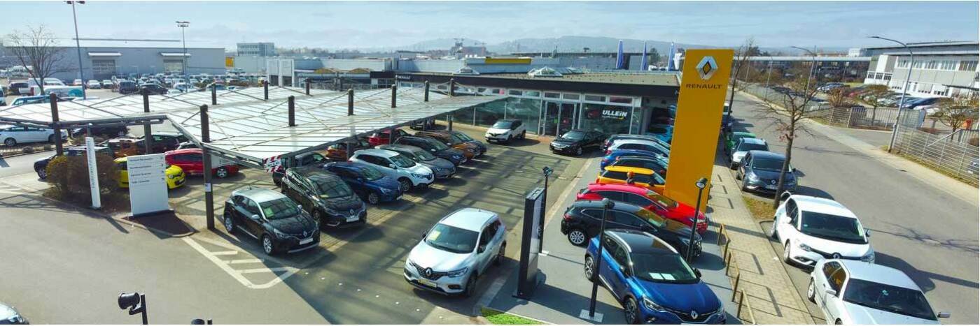 Renault Autohaus mit mehreren Fahrzeugen auf dem Parkplatz und modernem Verkaufsraum. Sonnenkollektoren im Vordergrund.