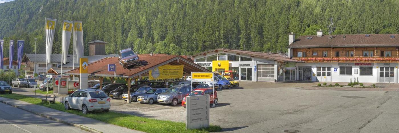 Autohaus mit mehreren Fahrzeugen, Verkaufsständen und einer bewaldeten Umgebung in den Alpen.