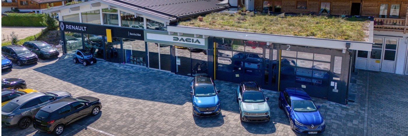 Renault und Dacia Autohaus mit grüner Dachlandschaft und geparkten Fahrzeugen auf dem Platz.