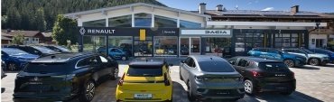 Autohaus mit Renault und Dacia Modellen, mehrere Fahrzeuge auf dem Parkplatz und ein klarer blauer Himmel.