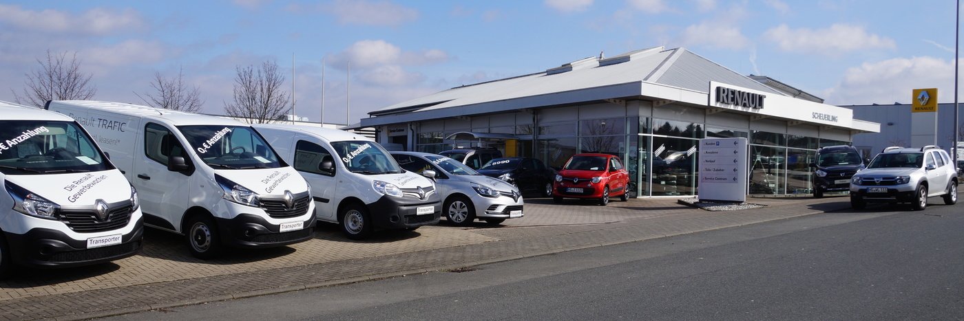 Fahrzeughandel mit mehreren Autos und Kleintransportern vor einem modernen Autohaus.