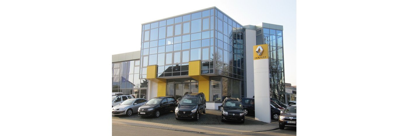 Autohaus mit moderner Glasfassade, Renault-Schild und parkenden Autos im Vordergrund.