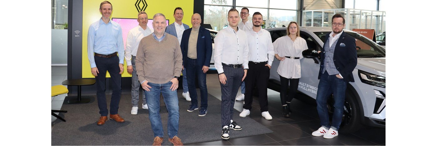 Gruppe von Fachleuten lächelt in einem Autohaus, umgeben von Autos, für ein Teamfoto.