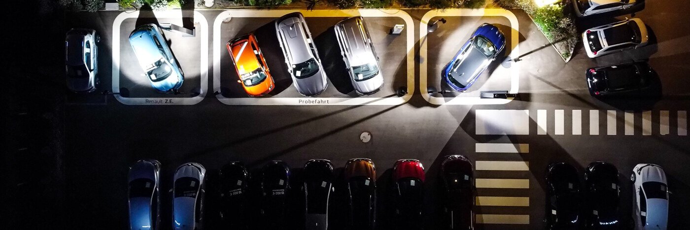 Überblick über einen Parkplatz bei Nacht mit mehreren geparkten Autos, einige beleuchtet.