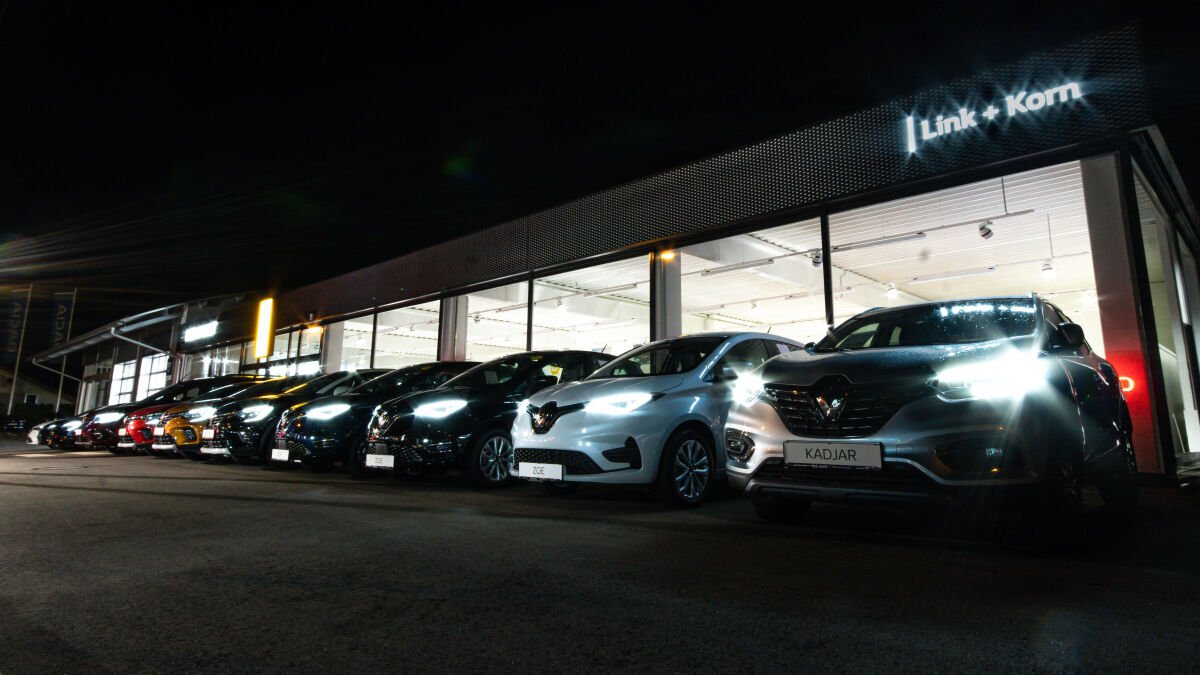 Eine nächtliche Aufnahme eines Autohauses mit einer Reihe von Renault-Modellen und beleuchteter Fassade.