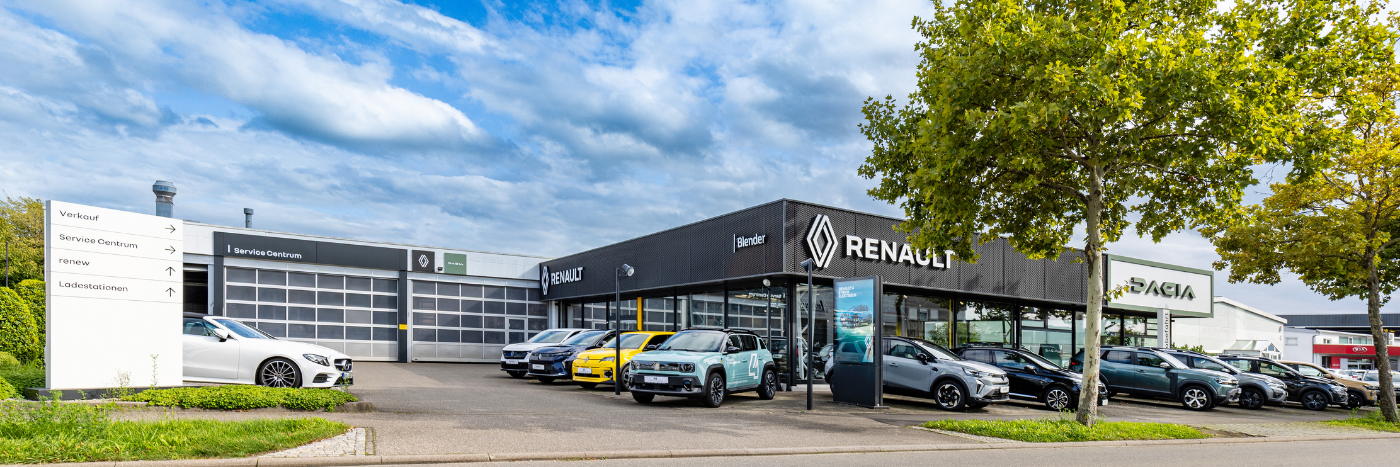 Renault Autohaus mit verschiedenen Fahrzeugen auf dem Parkplatz und blauen Himmel im Hintergrund.