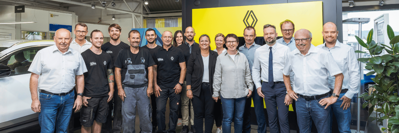 Gruppe von Mitarbeitern vor einem Renault-Logo in einem Automobilgeschäft, lächelnd und freundlich. 