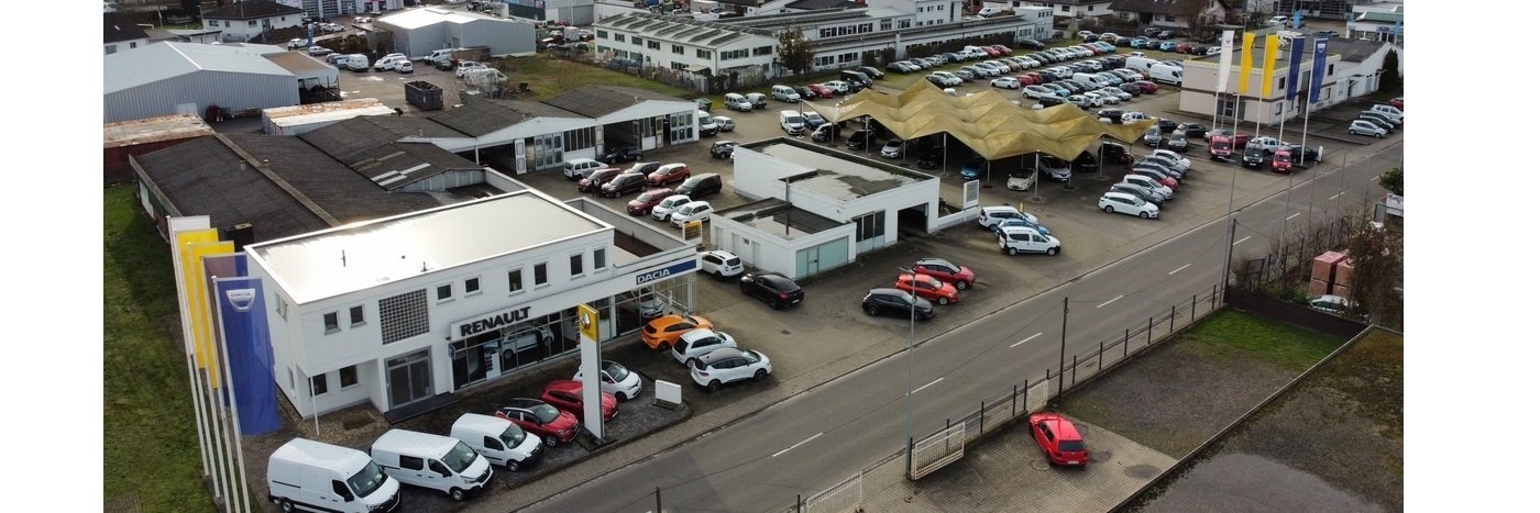 Luftaufnahme eines Autohandels mit verschiedenen Fahrzeugen und modernen Gebäuden.