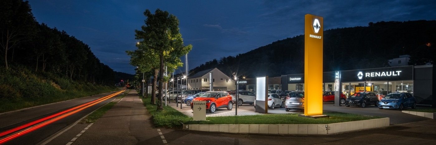 Renault Autohaus bei Nacht mit beleuchtetem Logo und mehreren Fahrzeugen auf dem Parkplatz.