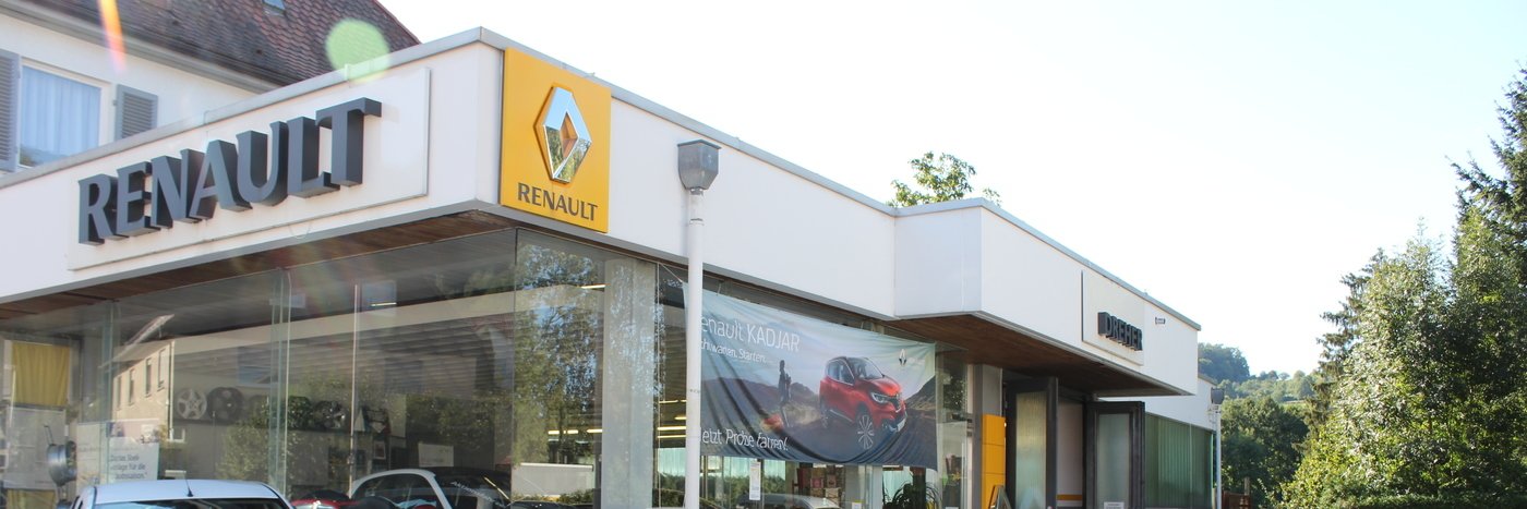 Renault Autohaus mit sichtbarem Logo und Schaufenster, umgeben von Bäumen und klarem Himmel.