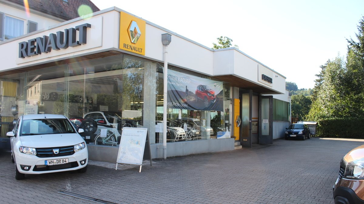 Renault Autohaus mit weißen Autos und Werbung in der Fensterfront, umgeben von folierten Bäumen.