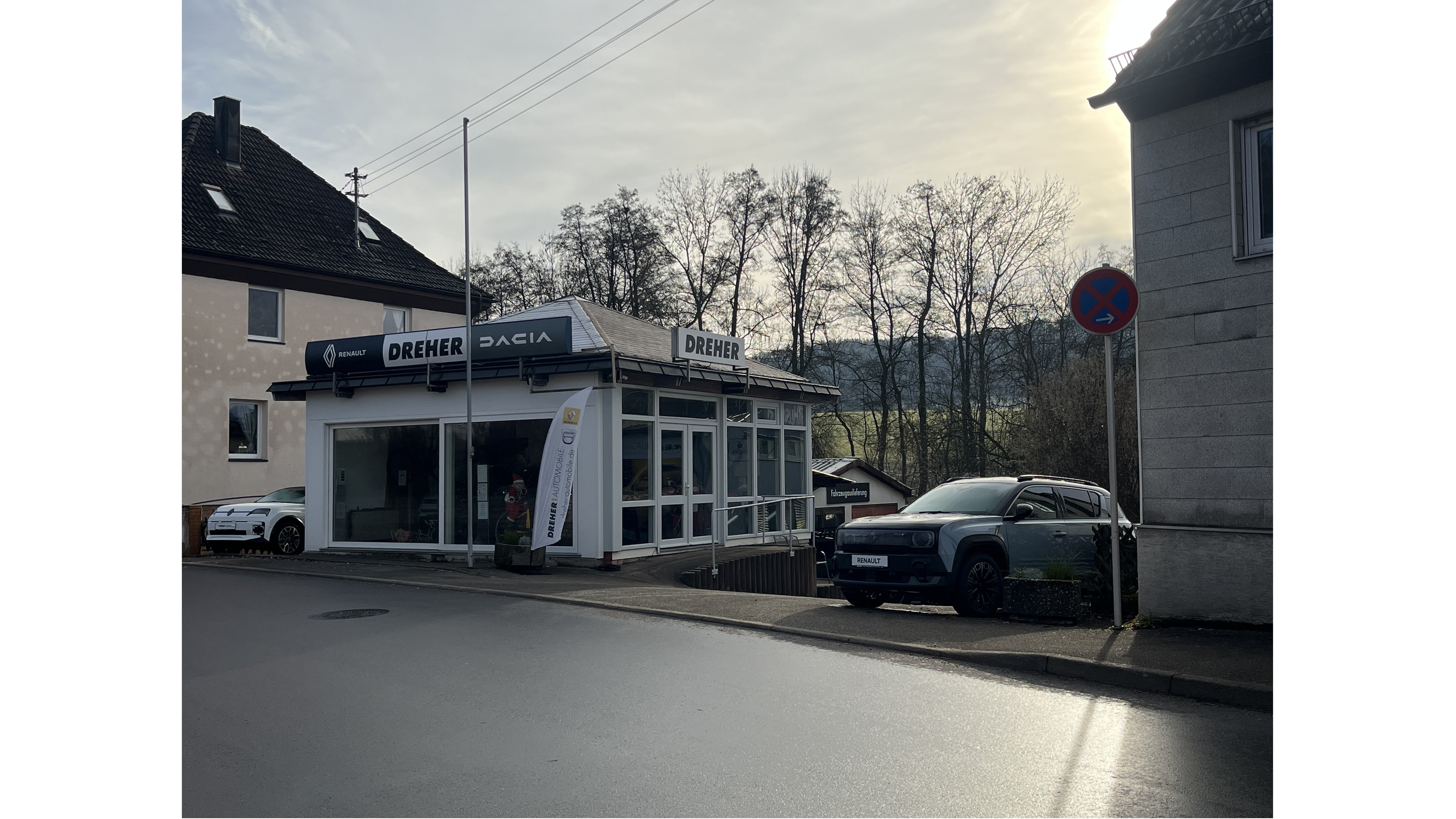 Autohaus Dreher mit Dacia-Modellen, umgeben von Bäumen und Parkverbotsschild in der Nähe.
