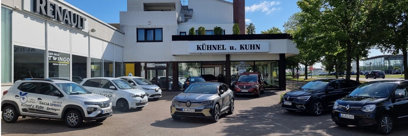 Autohandel Kühnel und Kuhn mit verschiedenen Renault-Fahrzeugen im Vordergrund, modernes Gebäude und klare Himmel.