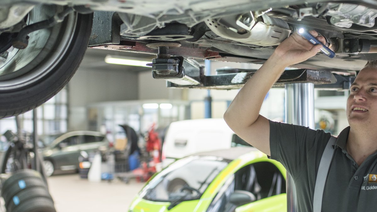Mechaniker überprüft ein Fahrzeug von unten in einer Werkstatt mit moderner Ausrüstung.