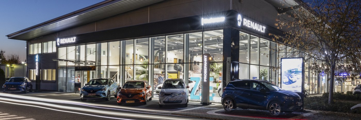 Renault Autohaus bei Nacht, mit mehreren Fahrzeugen vor der Glasfassade und Werbeanzeige.