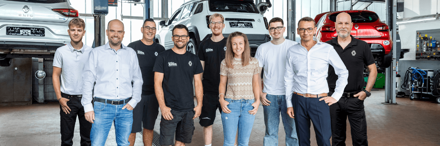 Ein Team von Mechanikern und Mitarbeitern in einer Autowerkstatt, mit Autos im Hintergrund.