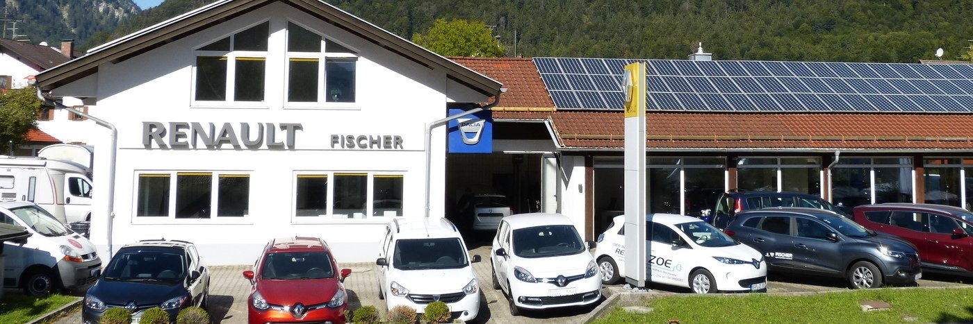 Renault Fischer Autohaus mit mehreren Autos auf dem Parkplatz, im Hintergrund Berge und Solarpanel.