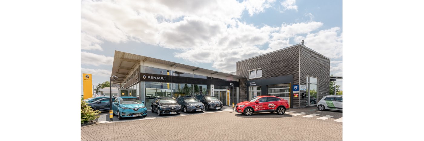 Renault Autohaus mit mehreren Fahrzeugen auf dem Parkplatz und modernem Gebäude unter bewölktem Himmel.