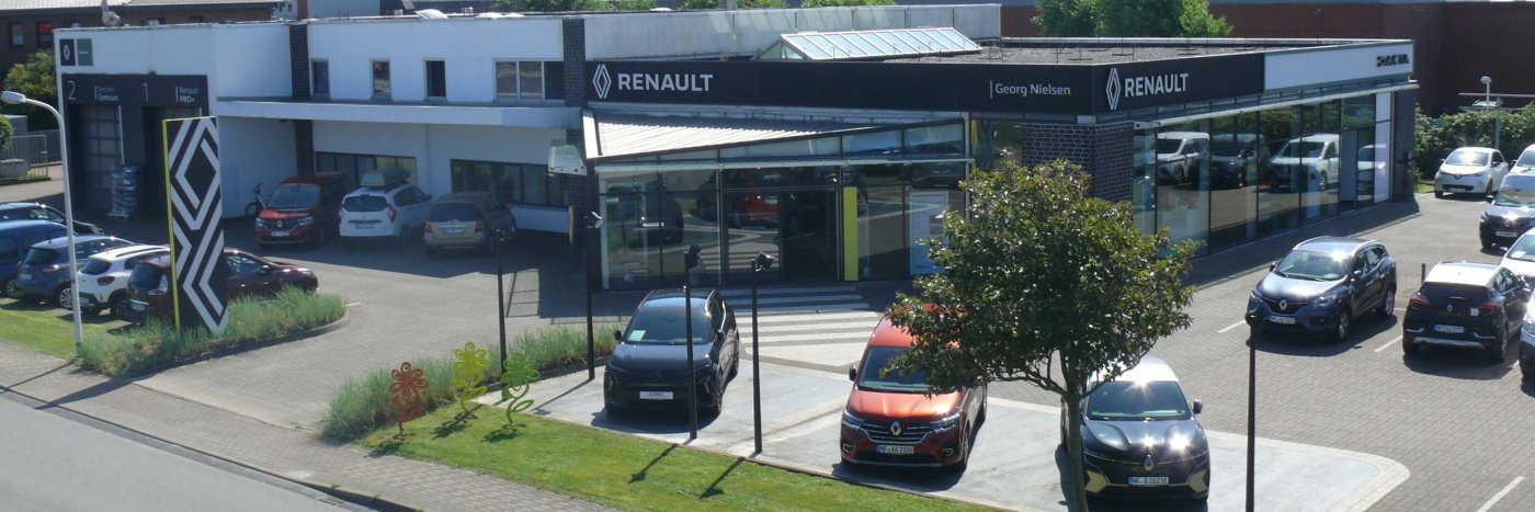 Renault Autohaus mit mehreren Autos und einer modernen Glasfassade, umgeben von grünen Flächen.