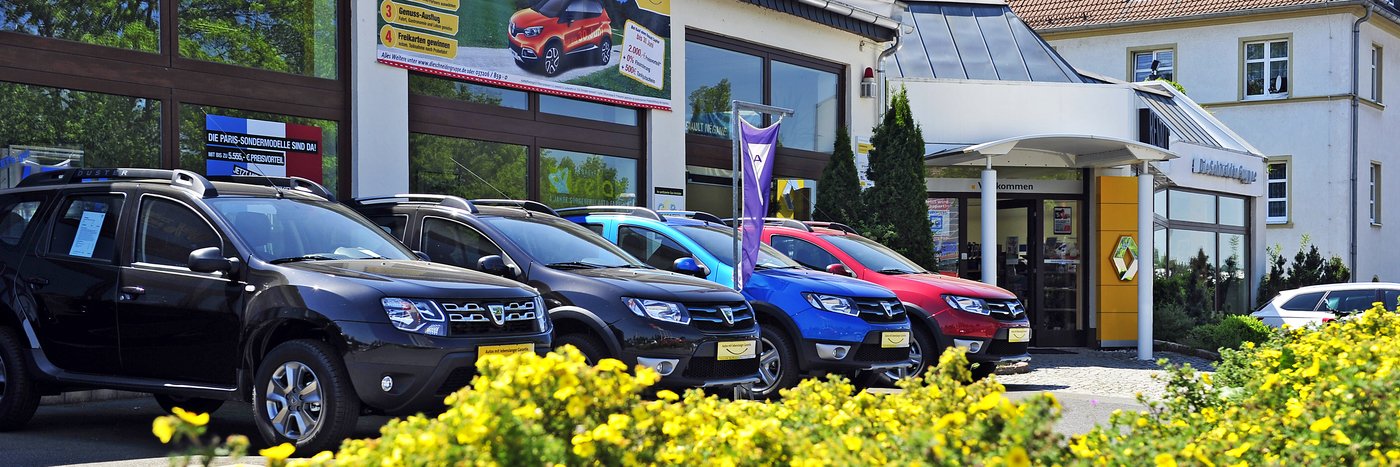 Autosalon mit mehreren SUV in verschiedenen Farben vor dem Eingang. Blumen im Vordergrund.