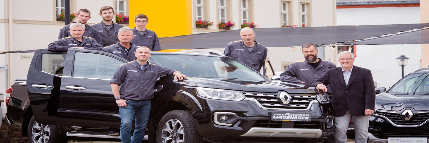 Gruppe von Fachleuten vor einem schwarzen Renault, im Hintergrund helle Gebäude mit Blumenfenstern.